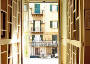 An open door leading to a balcony with a view of a building with multiple windows and shutters. - Butera Apartments Luxury (Palermo)