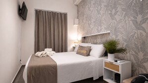 A neatly made bed with a brown blanket, a bedside lamp, a small potted plant, and a white nightstand with a woven basket. - Butera Apartments Luxury (Palermo)