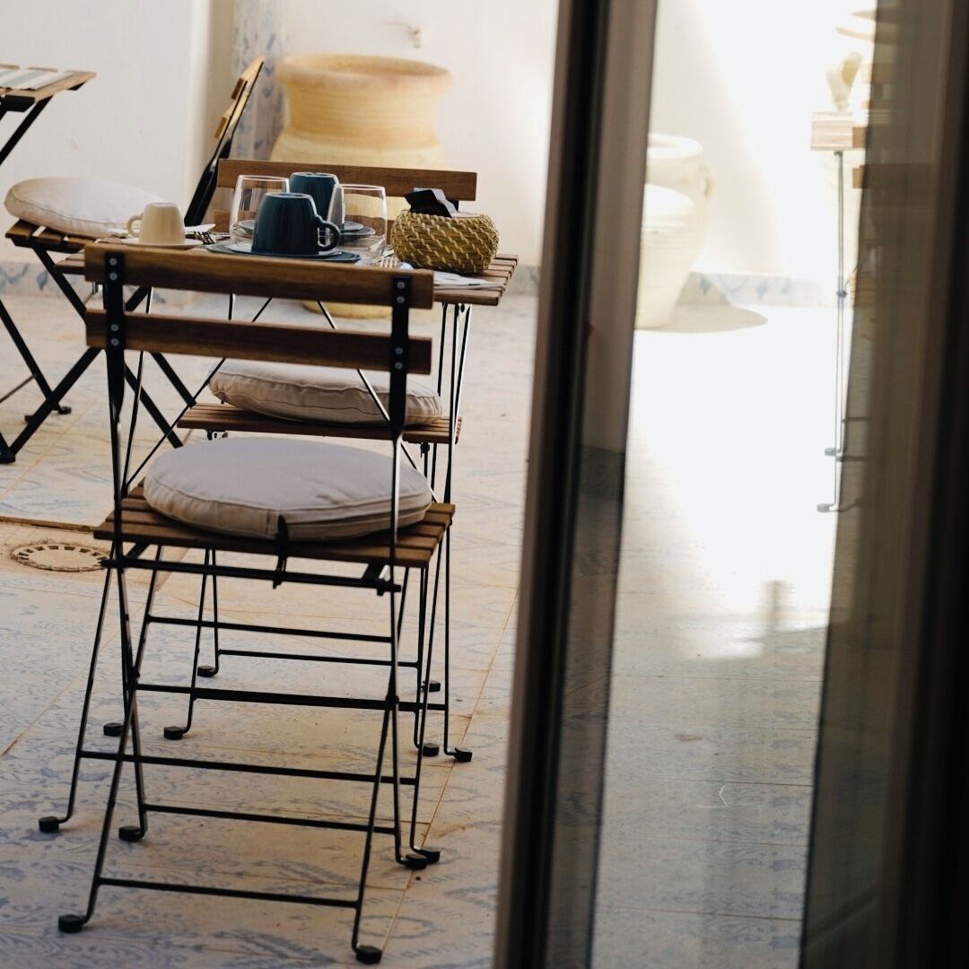 A room with a metal-framed table and chairs, a large woven basket, and a window with a view of the outside.