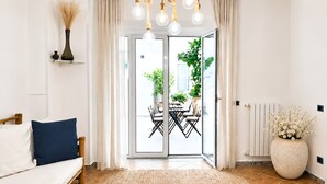 A modern living room with a sofa, a dining table with chairs, a large potted plant, and a sliding glass door leading to an outdoor area. - Butera Apartments Luxury (Palermo)