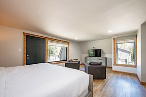 Une chambre à coucher comprenant un lit, un bureau, une chaise, un téléviseur et deux fenêtres.