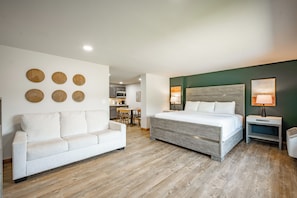 Une chambre d’hôtel avec un lit, un canapé blanc, un plancher en bois et, au fond, un coin repas.