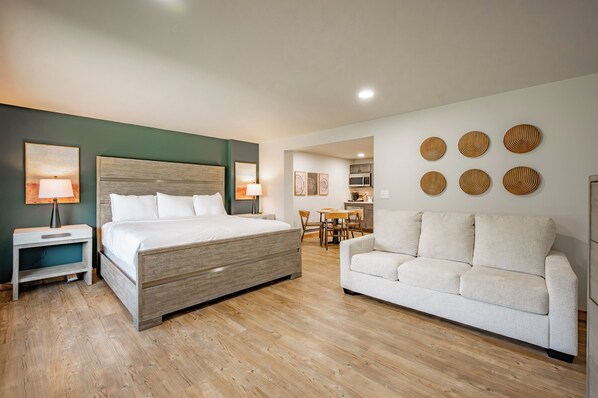 A bedroom with a bed, bedside tables, a sofa, a dining area, and wall decor.