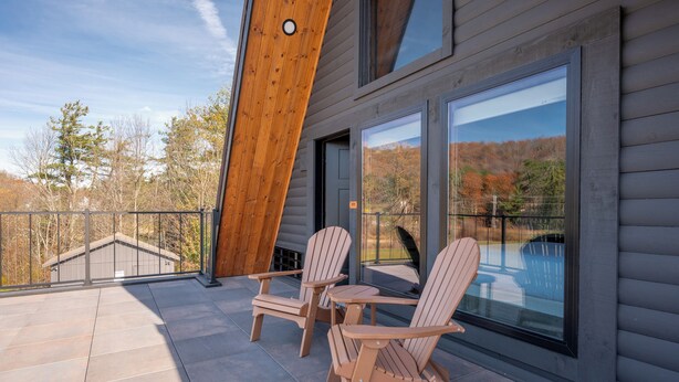 Un balcón con dos sillas Adirondack y una mesita, con vistas a un paisaje con árboles y una masa de agua.