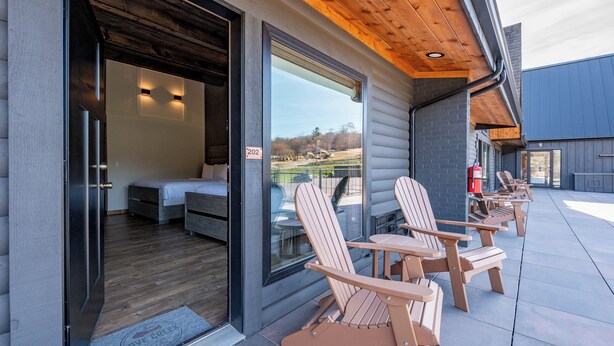 Een modern gebouw met een houten gevel, een glazen deur en een terras met Adirondack-stoelen.