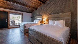 A bedroom with two beds, wooden ceiling beams, brick walls, and a view through a door. - Cove Creek Lodge: 203 Poolside Double Queen Room (Oakland)