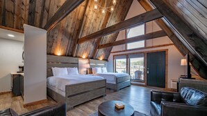 Una habitación amplia con techo alto, vigas de madera, una cama grande, un sofá, una mesita y una puerta que da a un balcón.