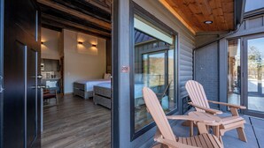 A modern log cabin with a cozy interior, a large sliding glass door, and two Adirondack chairs on the porch. - Cove Creek Lodge: 205 Poolside Double Queen Room (Oakland)
