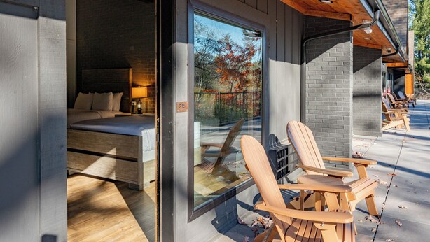 A modern room with a bed, a window, and two wooden chairs outside.