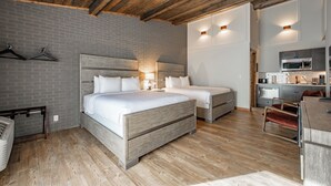 Un dormitorio con dos camas, techo de madera, pared de ladrillo y una kitchenette.