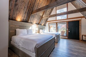 A bedroom with two beds, wooden beams, and a large window.