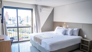 Une chambre d’hôtel moderne dotée d’un grand lit, d’une table de chevet, d’un bureau et offrant une vue sur la ville grâce à une grande fenêtre.