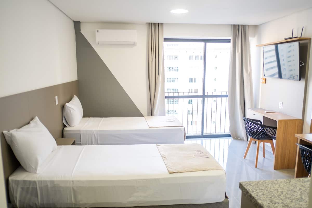 Une chambre d’hôtel avec deux lits, un bureau, une chaise, une télévision et un balcon donnant sur des immeubles.