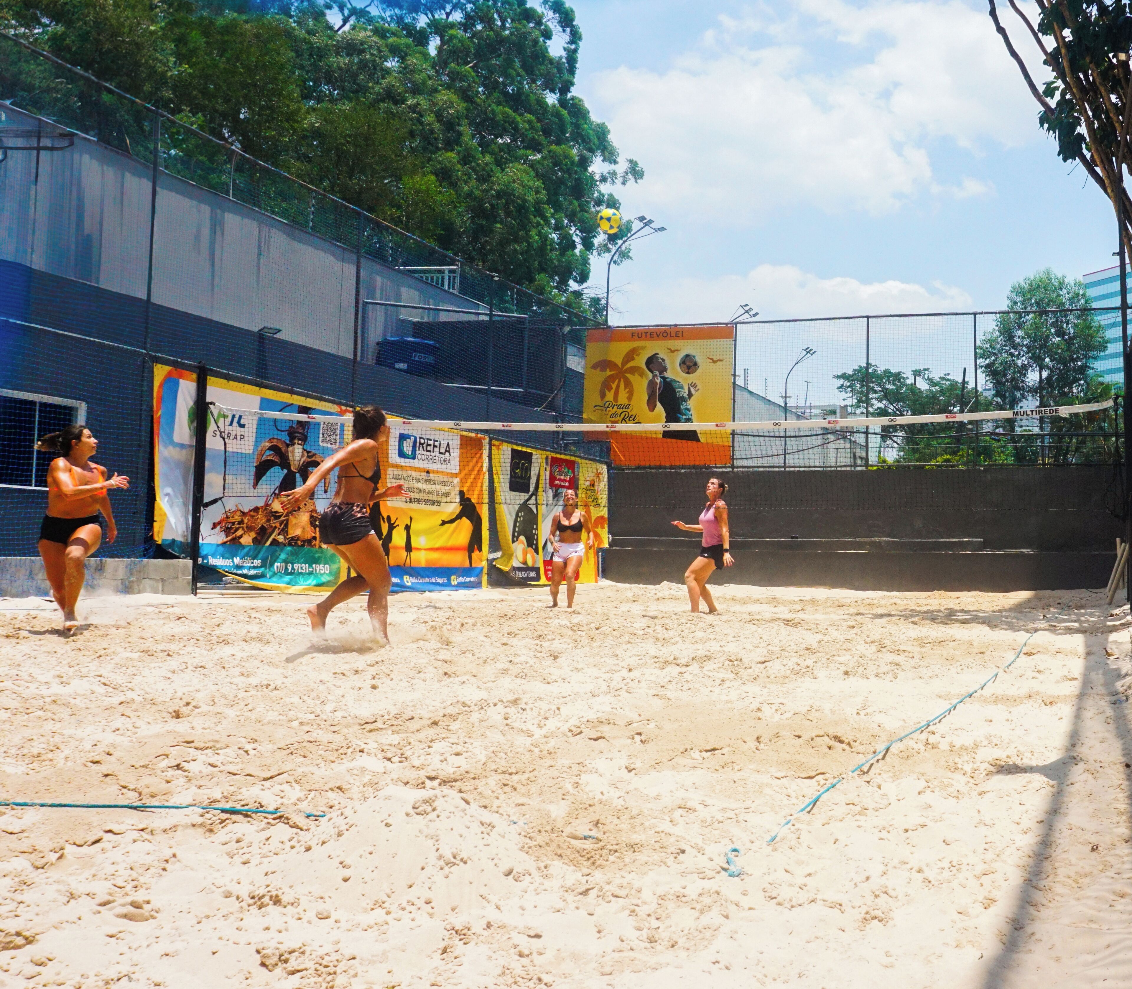 Jogo de voleibol numa quadra de areia com rede, cercada por outdoors.