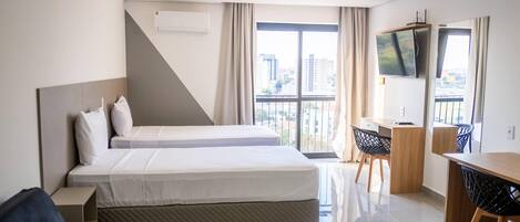 Habitación de hotel con dos camas, un escritorio, un televisor y un balcón con vistas a la ciudad.