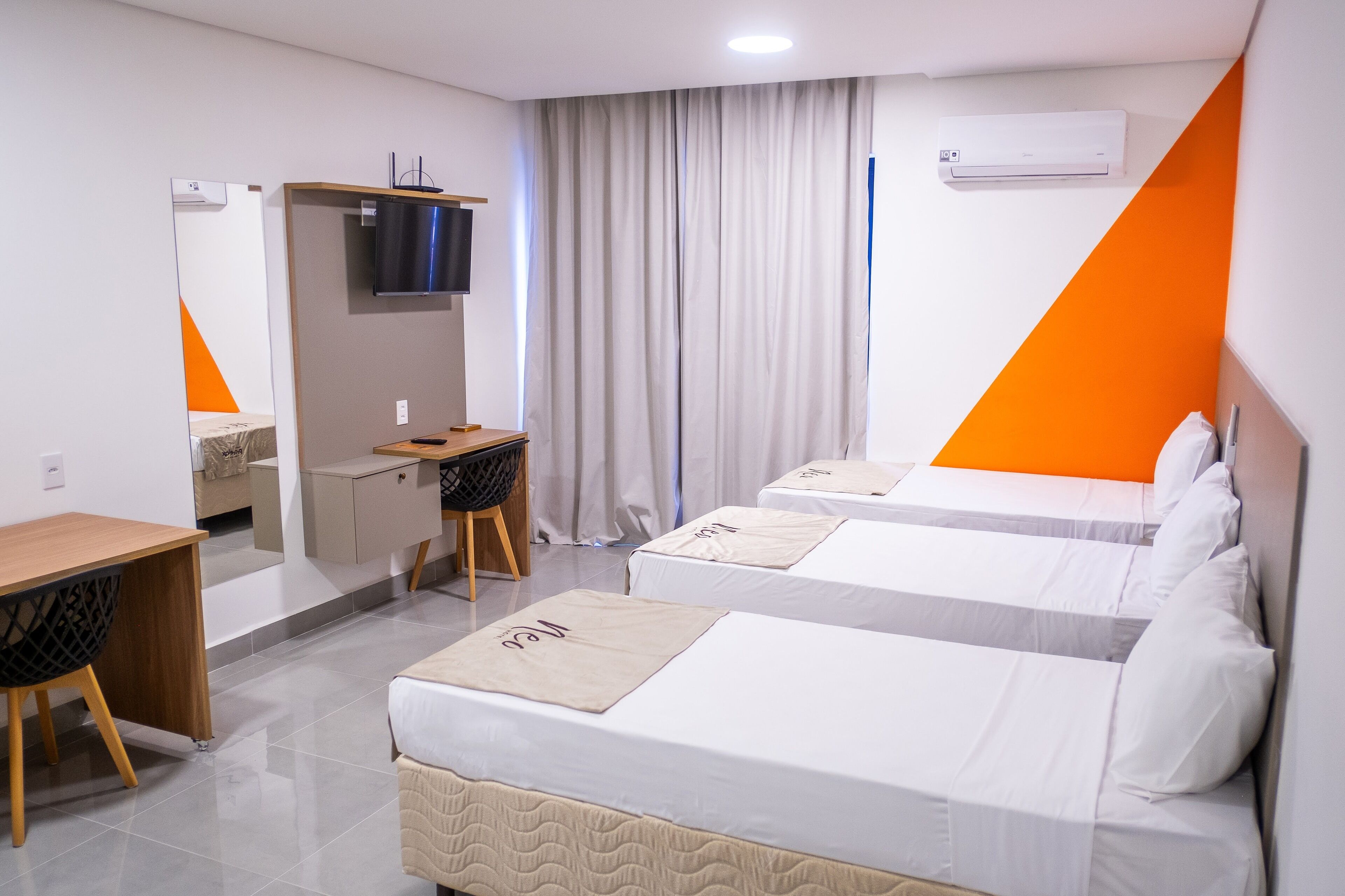 A hotel room with two beds, a desk, a chair, a TV, and an air conditioning unit.