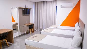 A hotel room with two beds, a desk, a chair, a TV, and an air conditioning unit.
