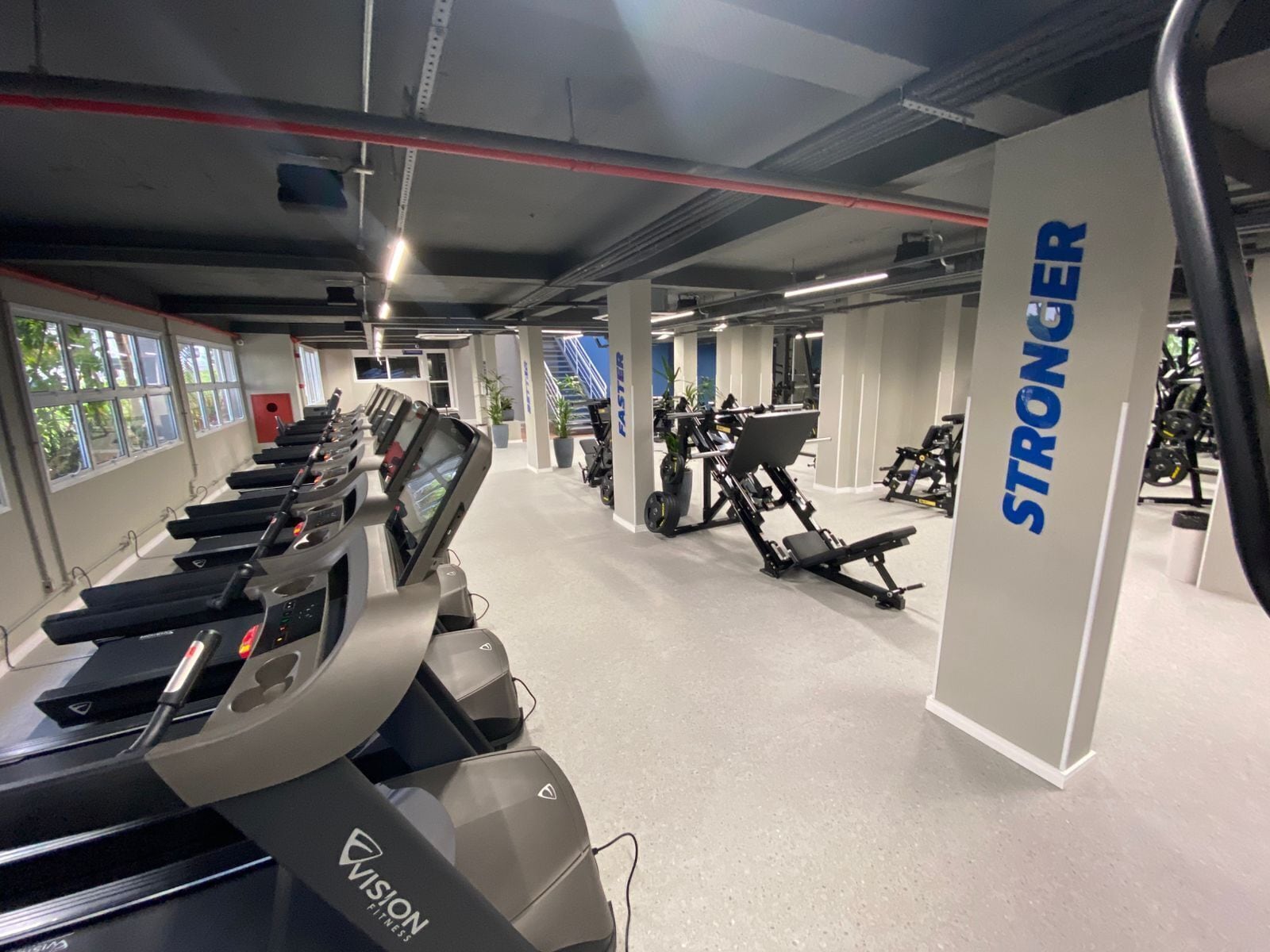 Ein Fitnessstudio mit Laufbändern, Kraftgeräten und einer Treppe.