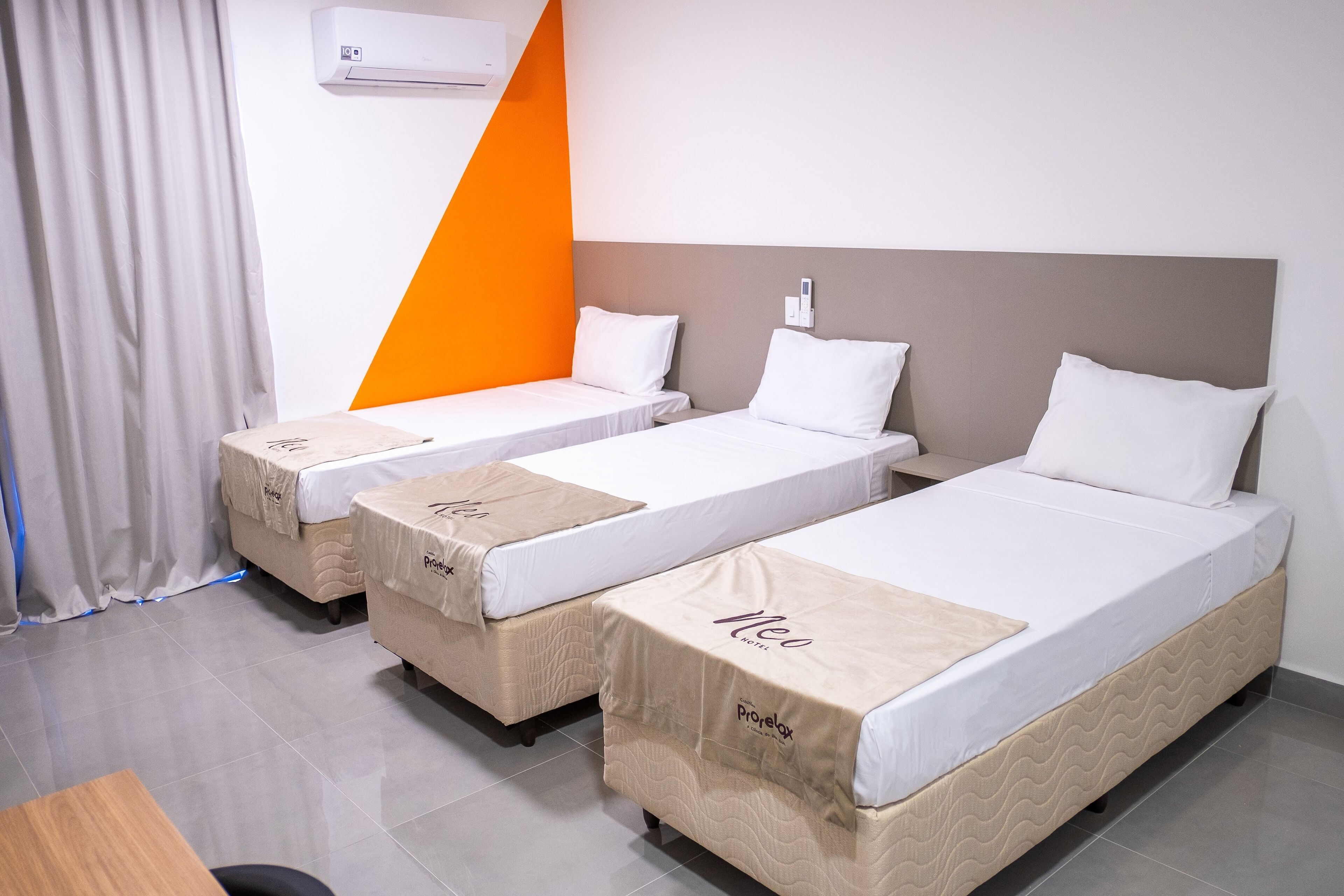 A hotel room with three single beds, a wooden desk, and a grey tiled floor.