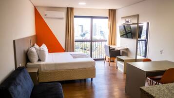 A hotel room with a bed, a desk, a TV, and a balcony with a city view.