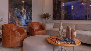 Un salón moderno con un cuadro abstracto grande, sillones de cuero, una mesa de centro redonda con objetos decorativos y un sofá de tonos neutros.