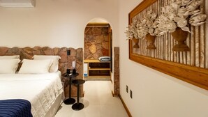Un dormitorio con pared de piedra, una cama con ropa de cama blanca, una mesita con un control remoto y un panel decorativo en la pared.