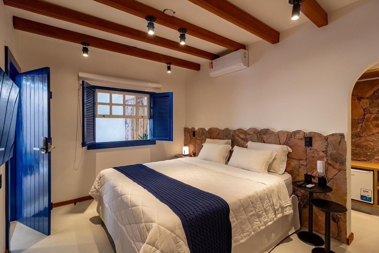 A bedroom with a large bed, a stone accent wall, a window with shutters, and a ceiling fan.