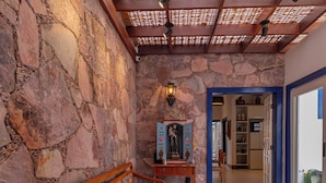 Una habitación con paredes de piedra, un banco de madera, una mesa con un florero y una estatua.