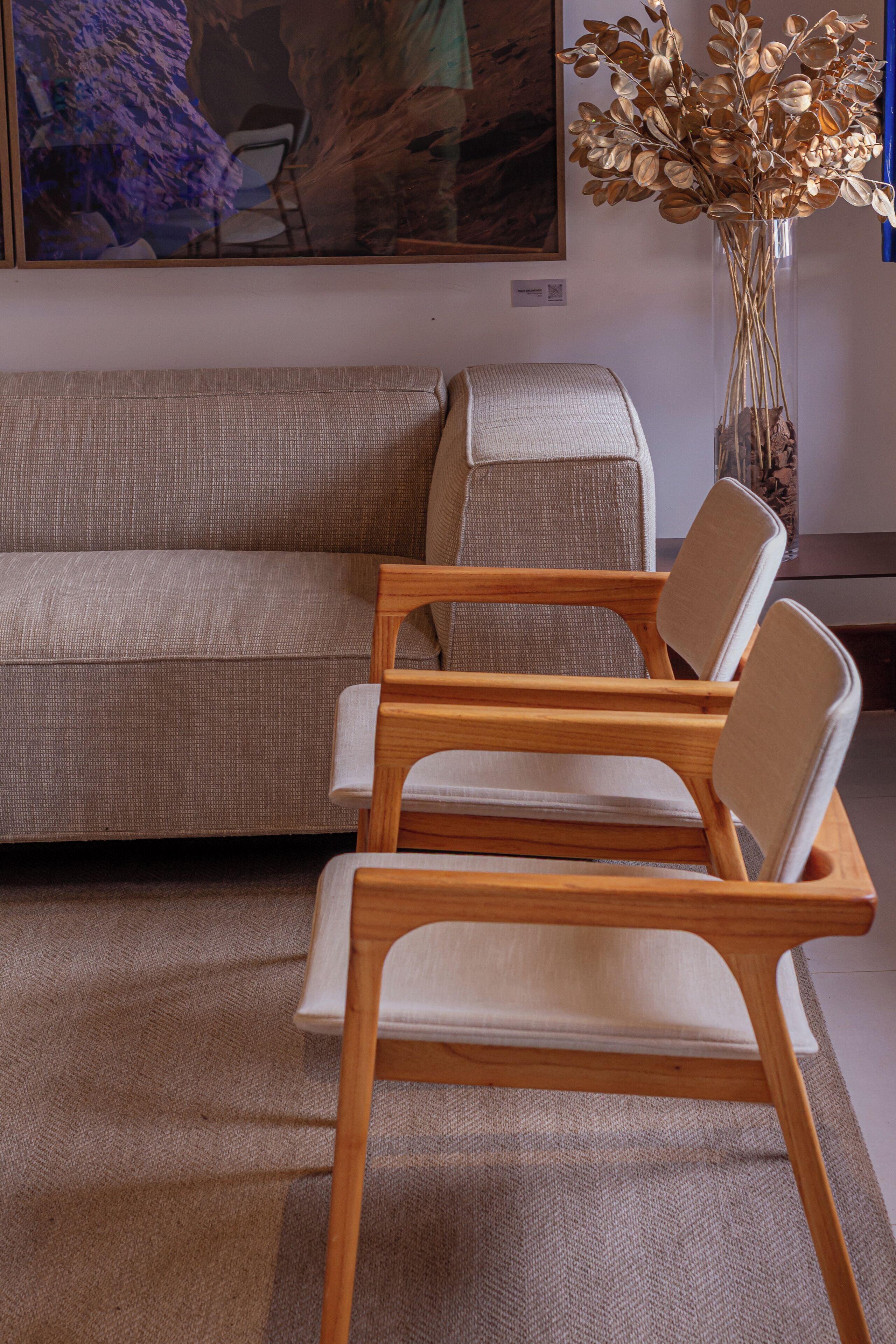 A modern living room with a beige sofa, wooden chairs, and a vase with dried flowers.