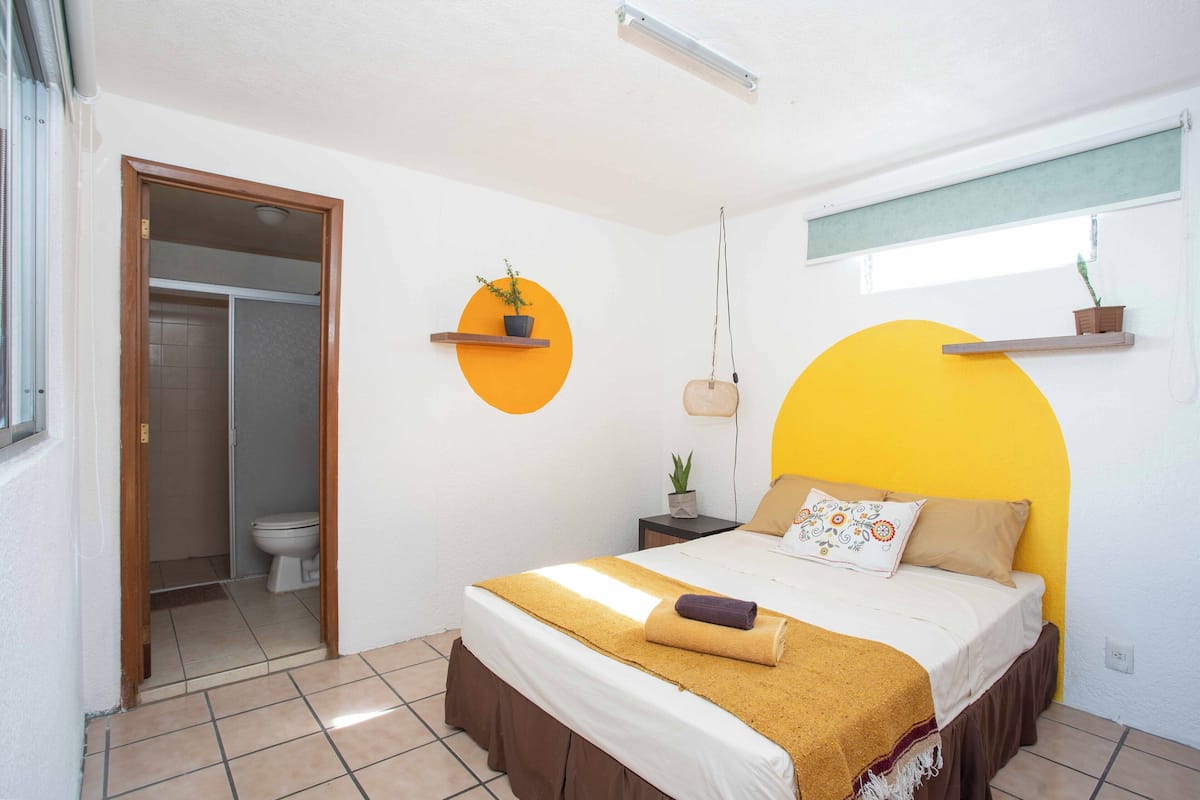 Ein Schlafzimmer mit Bett, Nachttisch, einer hängenden Pflanze und einem Fenster mit Blick.