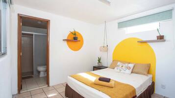 A bedroom with a bed, a bedside table, a hanging plant, and a window with a view.