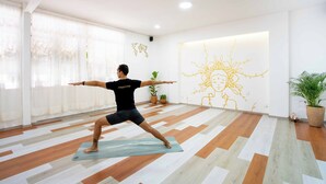 A person performing a yoga pose on a mat in a room with a patterned floor, large windows, and a wall with a sun design. - La Paz & Love Hostel (Guadalajara)