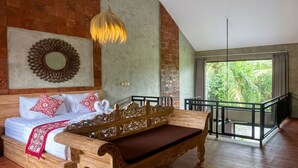 A bedroom with a bed, a wooden bench, a hanging light fixture, a decorative mirror, and a balcony with a view of greenery. - Juminten Villa  (Ubud)