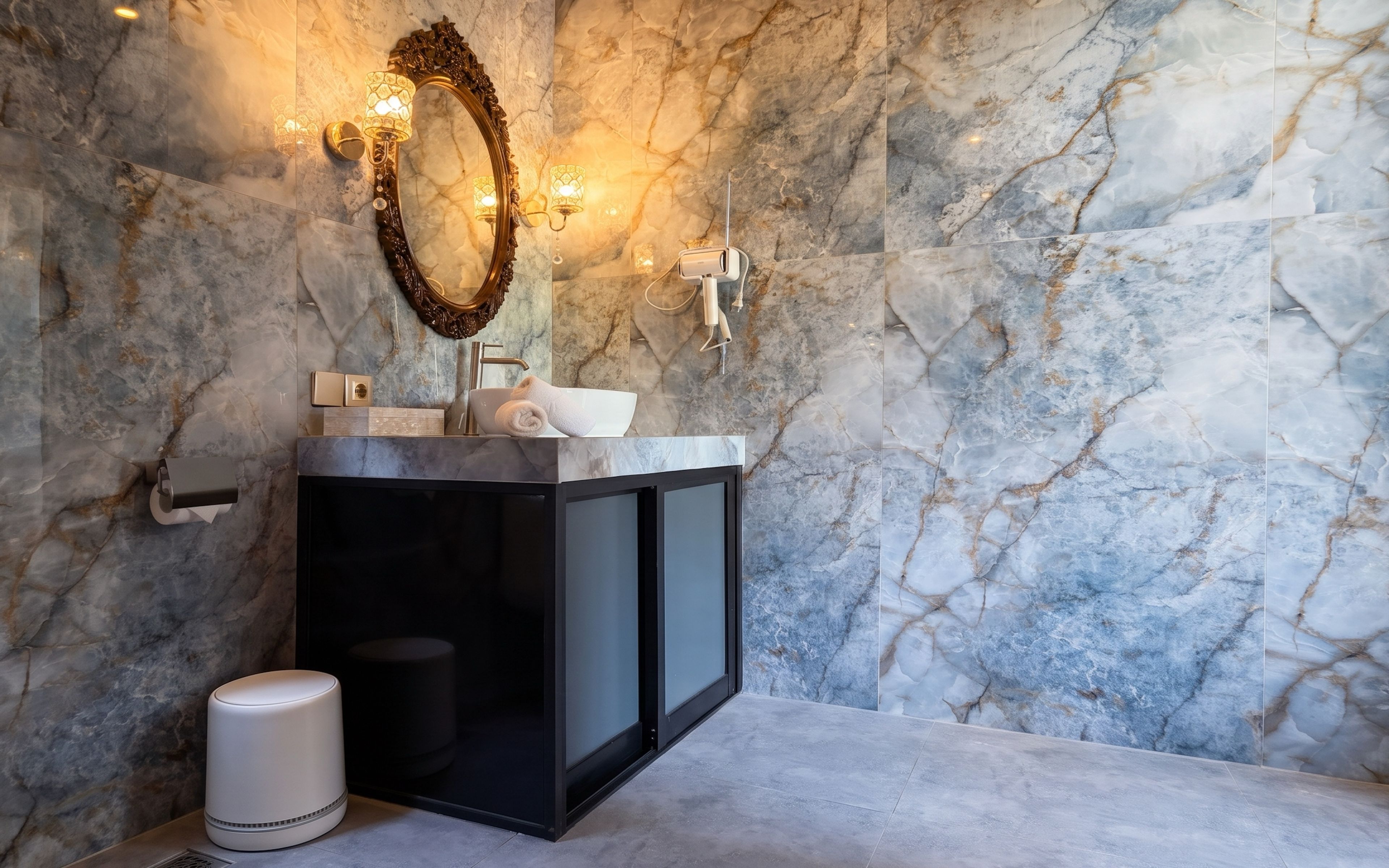 A bathroom with a marble wall, a black cabinet, a mirror with a decorative frame, and a towel on the sink.