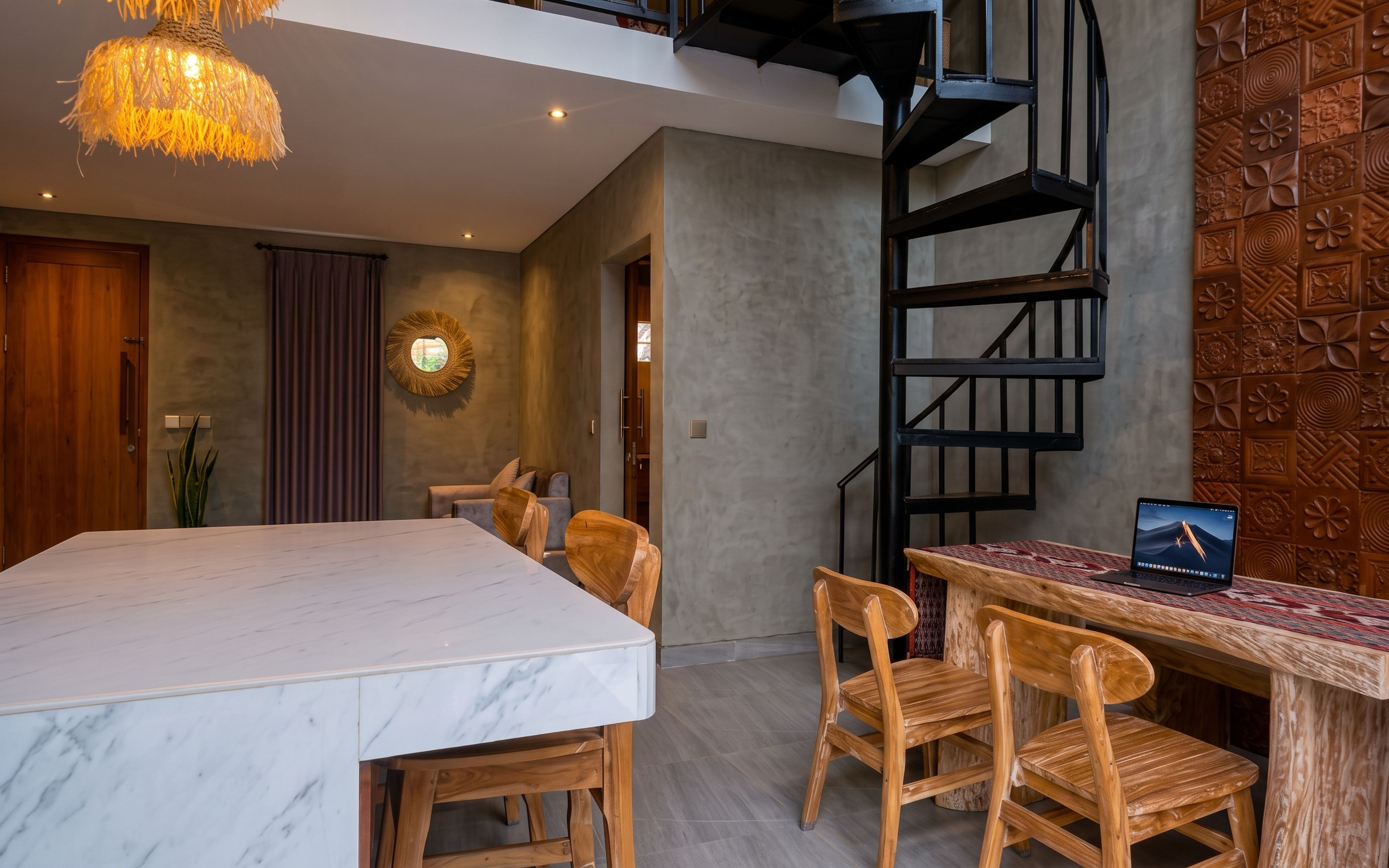 A modern interior with a marble dining table, wooden chairs, a spiral staircase, and a laptop on a wooden desk.