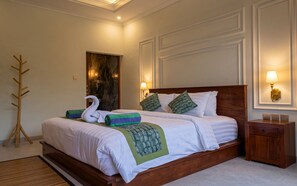 A hotel room with a wooden bed, a green and white patterned throw, a swan-shaped towel, and a wooden coat rack. - Juminten Villa  (Ubud)