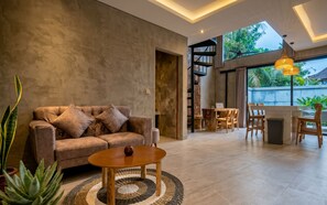 A modern living room with a sofa, coffee table, and a dining area with wooden chairs and a table. - Juminten Villa  (Ubud)