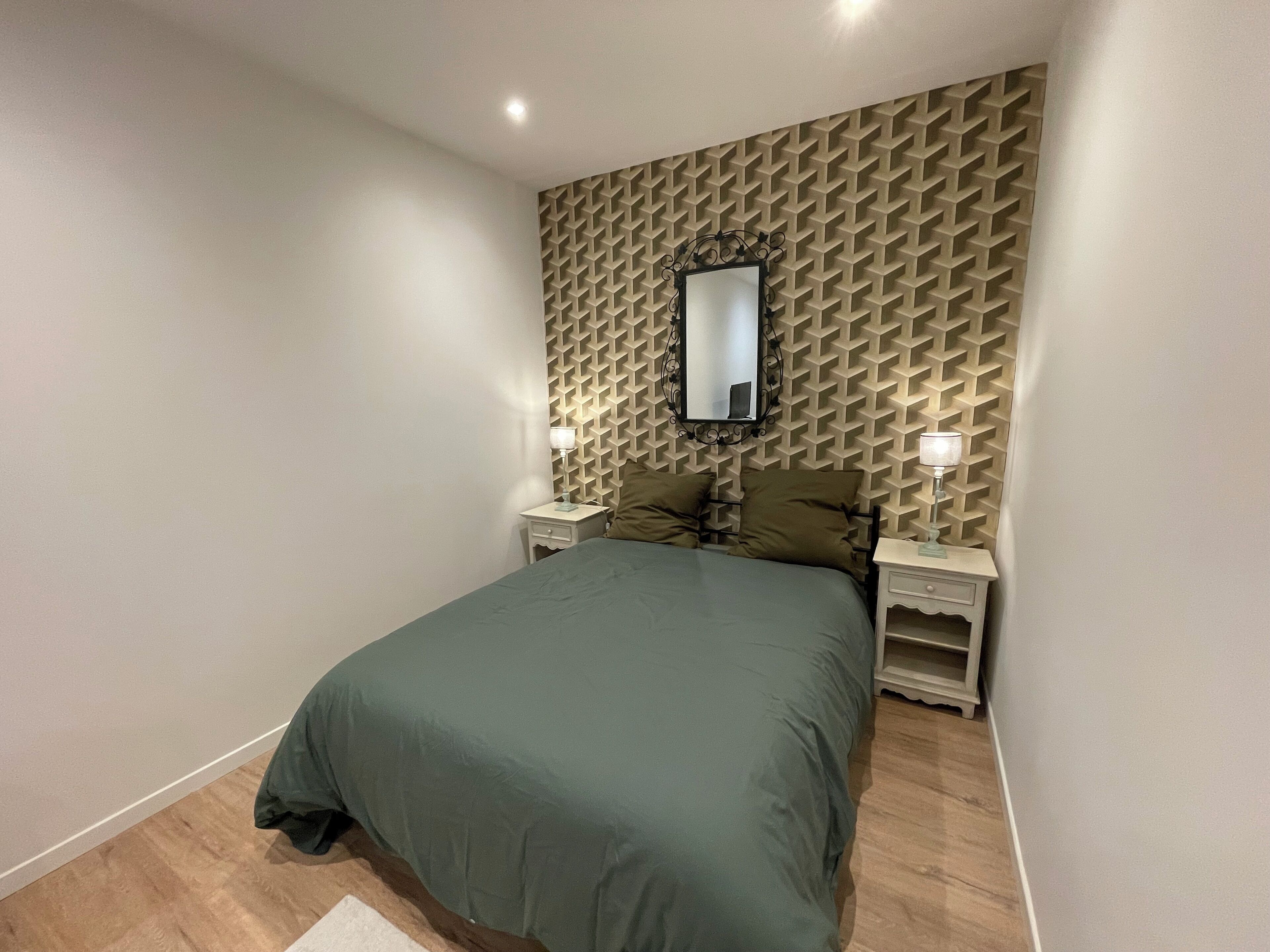 Ein Schlafzimmer mit einem Bett, zwei Nachttischen, einem Spiegel und einer Wand mit Muster.