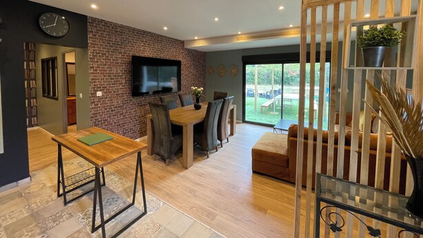 Een moderne woonkamer met een bakstenen muur, een flatscreen televisie, een houten eettafel en een bank.