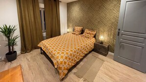 Een moderne slaapkamer met een bed met een patroon, een nachtkastje met een lamp, een potplant en een deur.