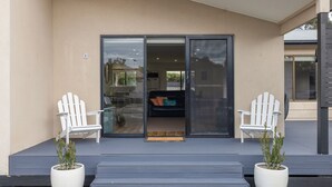 A modern building entrance with a glass door, two white Adirondack chairs, and potted plants.