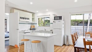 A modern kitchen with white cabinetry, a central island with stools, a microwave, and a refrigerator.