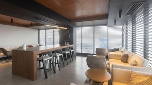 Een modern interieur met een bar in het midden, zitgedeeltes en grote ramen voor natuurlijk licht.