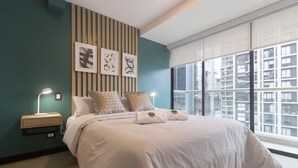 Een moderne slaapkamer met een groot bed, twee bedlampen en een stadszicht door een groot raam.