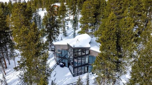 Un chalet moderne entouré d’arbres et de montagnes enneigées.