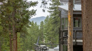 Une terrasse en bois, agrémentée de mobilier d’extérieur, entourée d’arbres et offrant une vue sur une montagne.