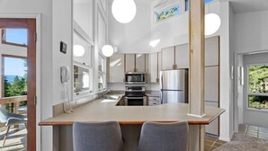 Une cuisine moderne avec un îlot central, deux chaises grises, un réfrigérateur en acier inoxydable et un four à micro-ondes.
