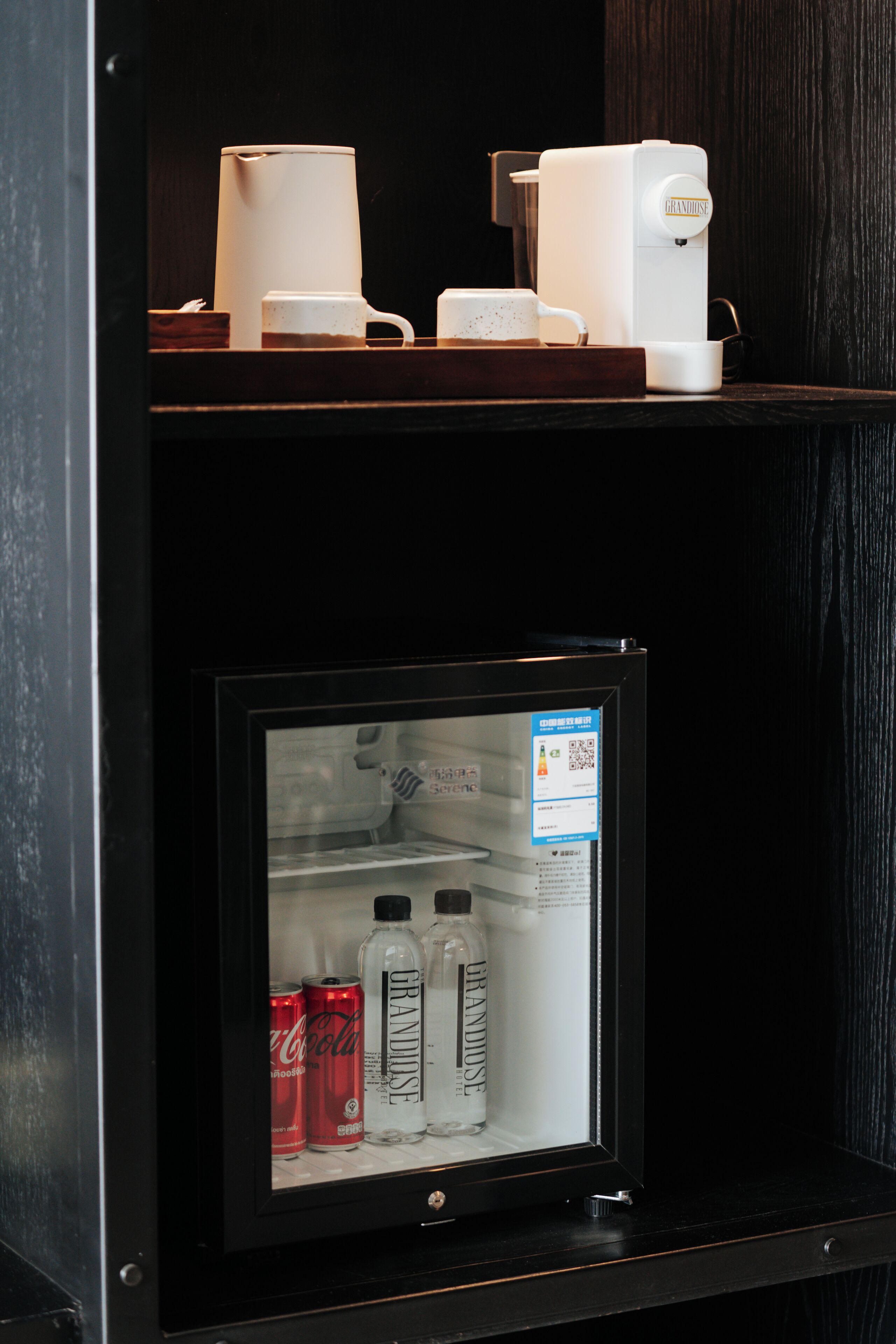 Un miniibar con un refrigerador que contiene bebidas y una cafetera.