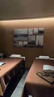 A room with two beds, a wall with multiple framed pictures, and a small table with a plant.