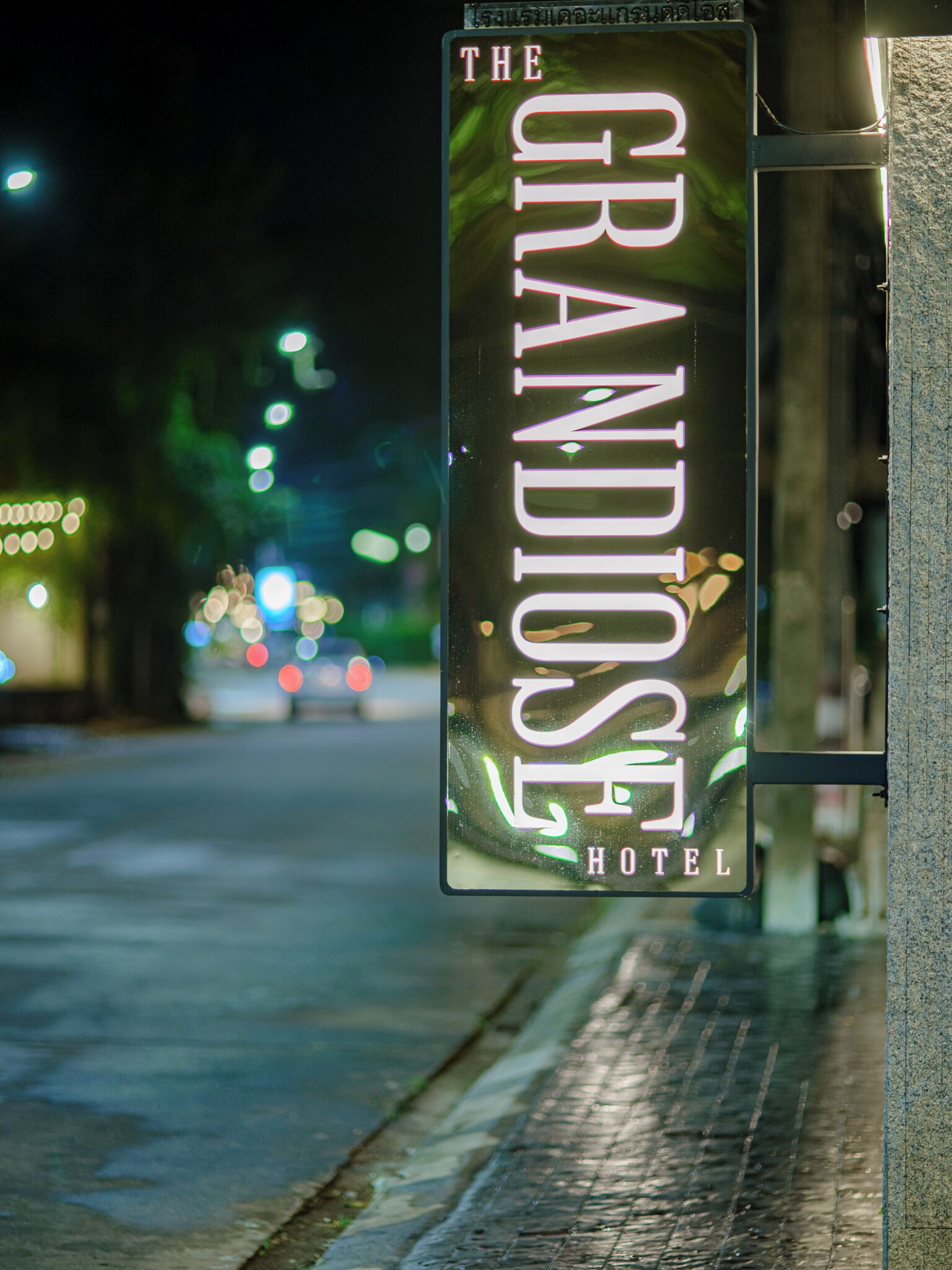 Een nachtelijk bord voor Hotel The Grandiose, met verlichte tekst en een gedeeltelijk zicht op de gevel van het gebouw.